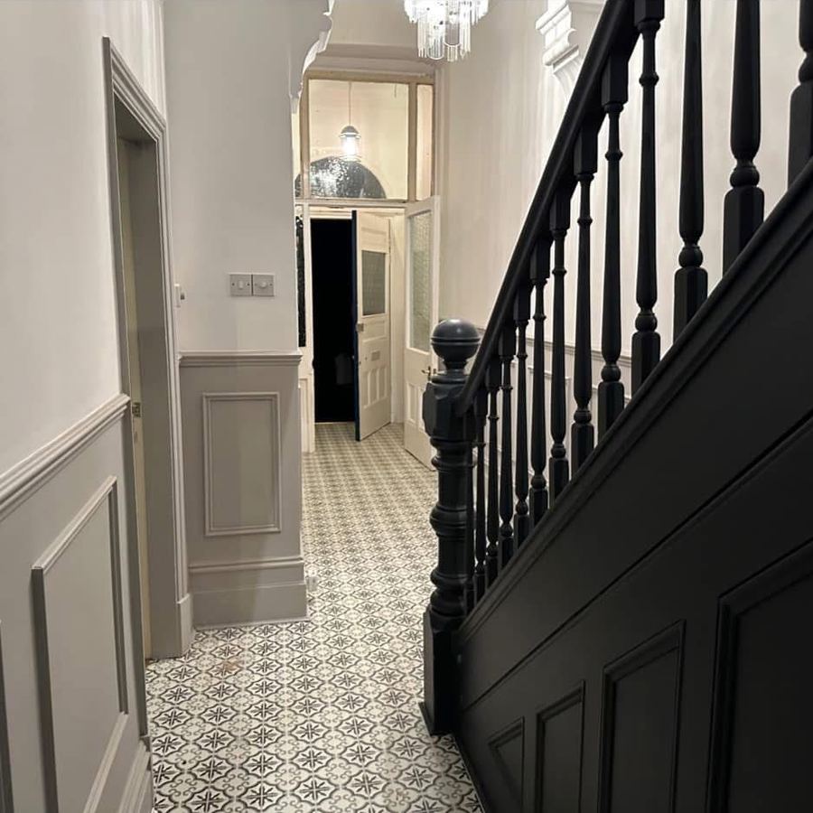 Restored hallway with dark painted banister, panelling and patterned tile floor